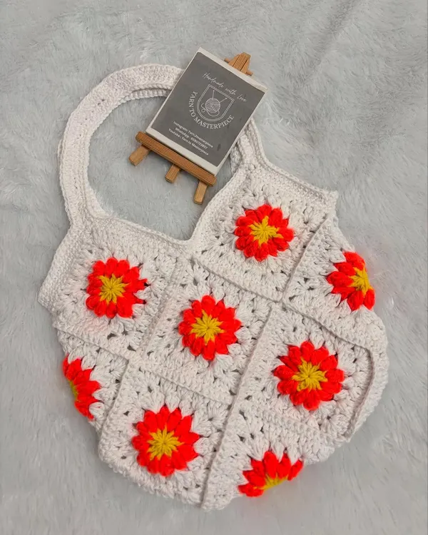 This shoulder bag is made from white granny squares, each featuring a vibrant sunflower design. It's a cheerful and stylish accessory, perfect for adding a pop of color to your look.