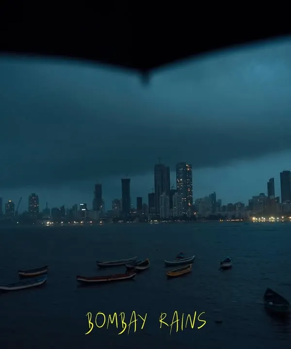 A classic Bombay rain scene, viewed from under an umbrella. The dark, moody sky and distant city lights create a feeling of quiet contemplation amidst the vastness of the sea.