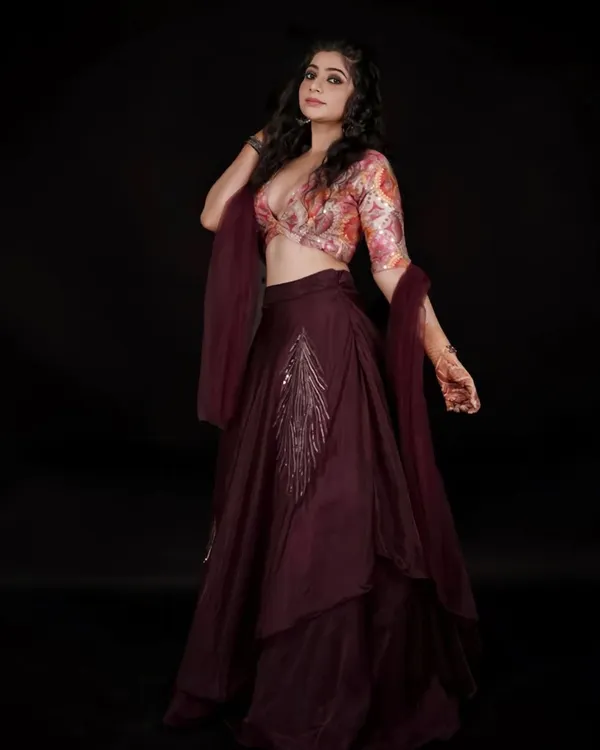 This stylish party-wear lehenga features a floral print crop top and a deep wine-colored asymmetrical skirt. The silver embroidery on the skirt adds a touch of elegance, making it a great rental for a cocktail party or reception.