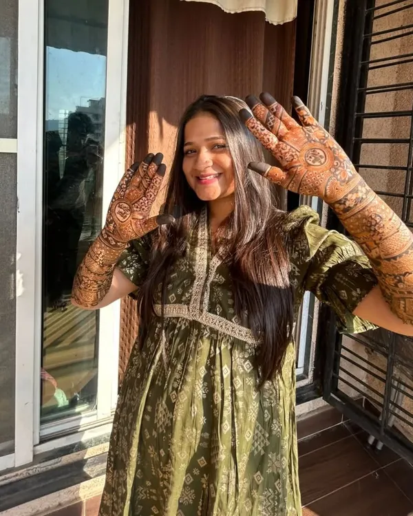 A happy bride basking in the sun, showing off her full bridal mehndi. Her smile says it all, and the natural light beautifully highlights the rich color of the stain.