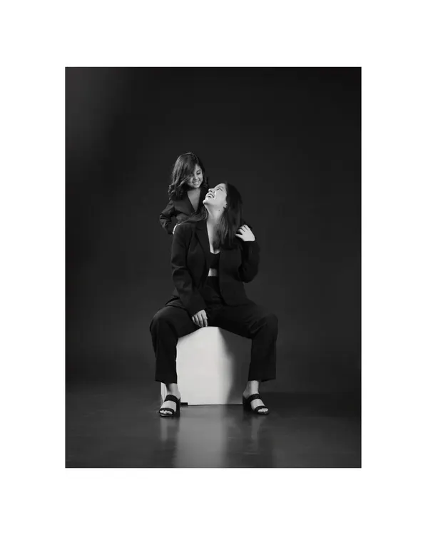 A mother and daughter, dressed in matching black suits, share a laugh against a dark, moody background. This classic black and white style creates a powerful, dramatic portrait of their joyful bond.