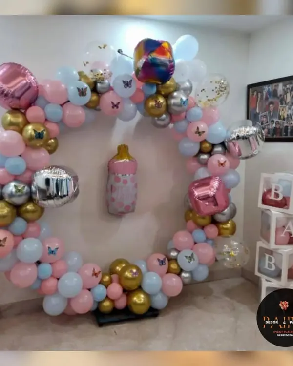 A beautiful ring decoration for a birthday party. This setup features a mix of pink, blue, gold, and silver balloons, with "BABY" blocks and butterfly accents.