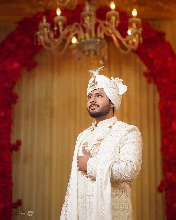 A portrait of the groom, looking sharp and regal in his ivory sherwani. The elegant decor and lighting highlight his sophisticated wedding day look.