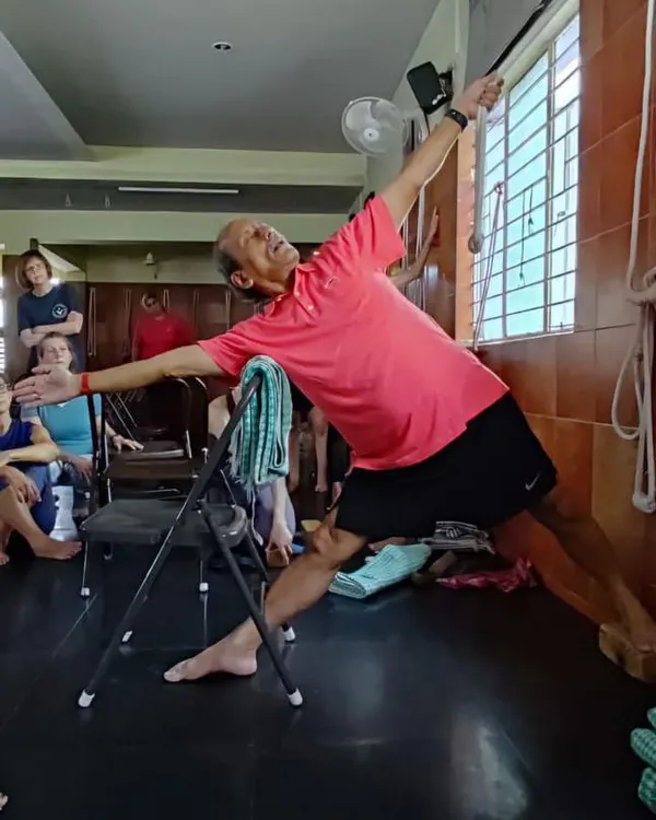Here, I am demonstrating Utthita Trikonasana, or Triangle Pose, using a chair and ropes to help deepen the stretch and maintain correct alignment. This is a core principle of Iyengar yoga, where props assist in exploring the asana safely.