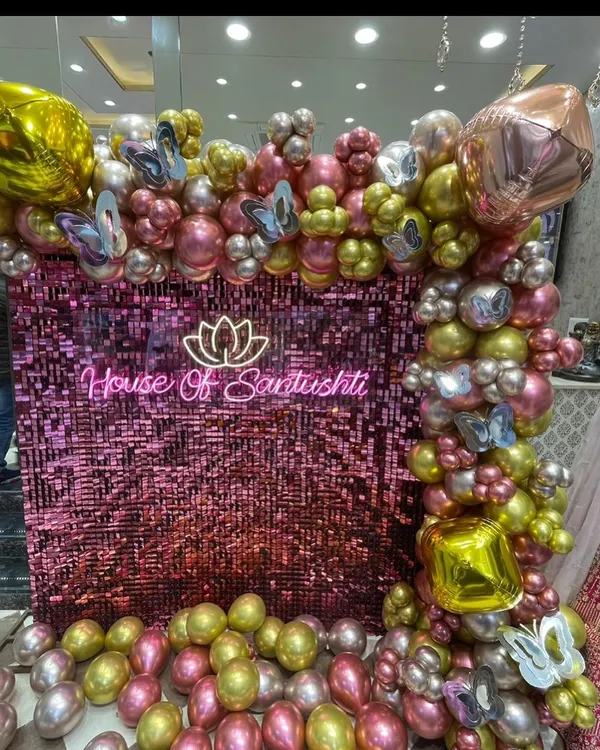 A stunning photo-op corner for a brand launch, featuring a shimmering pink sequin wall with a custom neon logo. The scene is framed by an elaborate organic garland of chrome pink, gold, and silver balloons, creating a luxurious and highly photogenic brand activation experience.