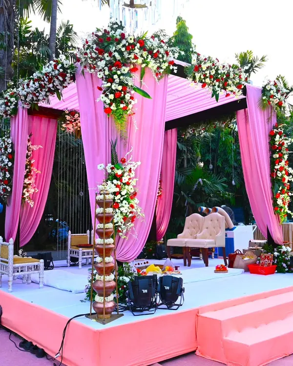 A beautiful sundowner wedding mandap at The Acres Club. The pink drapes and heavy floral arrangements with red and white flowers create a romantic and vibrant setting for the ceremony.