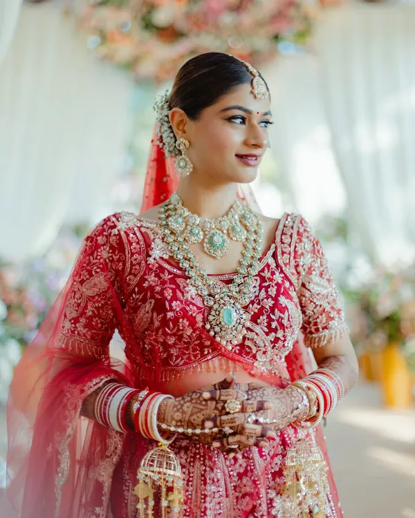 A beautiful portrait of my bride Mansi, looking radiant for her pheras. The look features a classic red lip, defined eyes, and a clean, elegant bun, perfectly complementing her stunning red lehenga and polki jewelry.