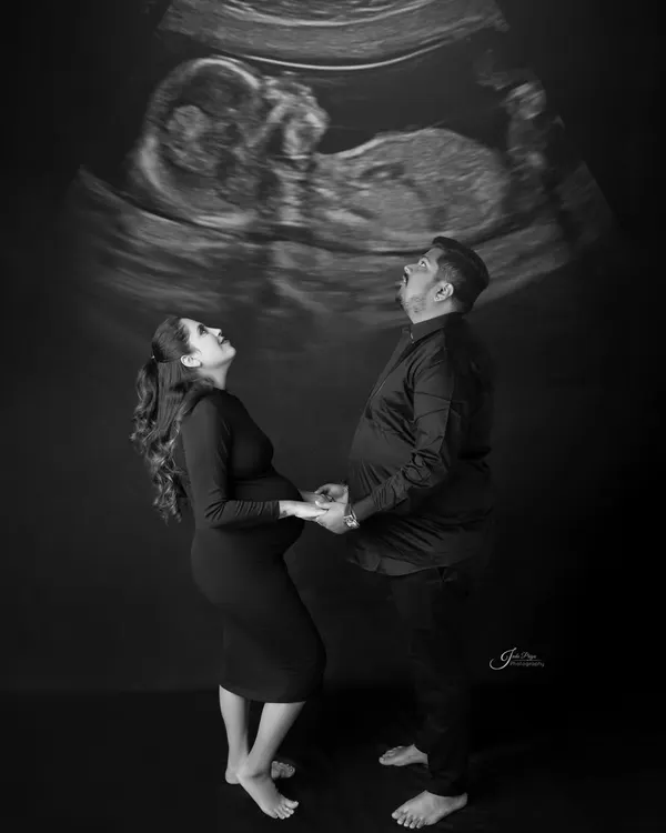 A creative and striking black and white portrait. The couple looks up in awe at their baby's sonogram, which is projected above them, creating a unique and meaningful image.