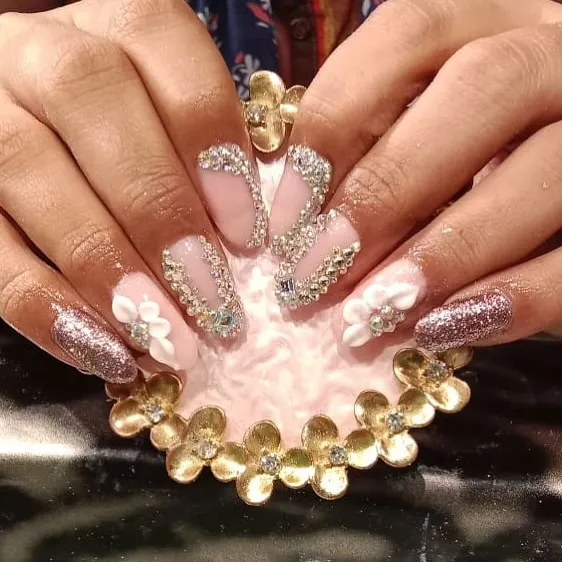 A truly extravagant set of stiletto nail extensions featuring 3D white flowers, rose gold glitter, and intricate rhinestone patterns. This is perfect for a bridal or special occasion look.