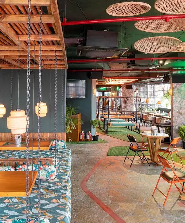 A wide shot of the jungle-themed Social Offline in Gurugram. This photo captures the eclectic mix of seating, including the unique swing chairs and vibrant murals.