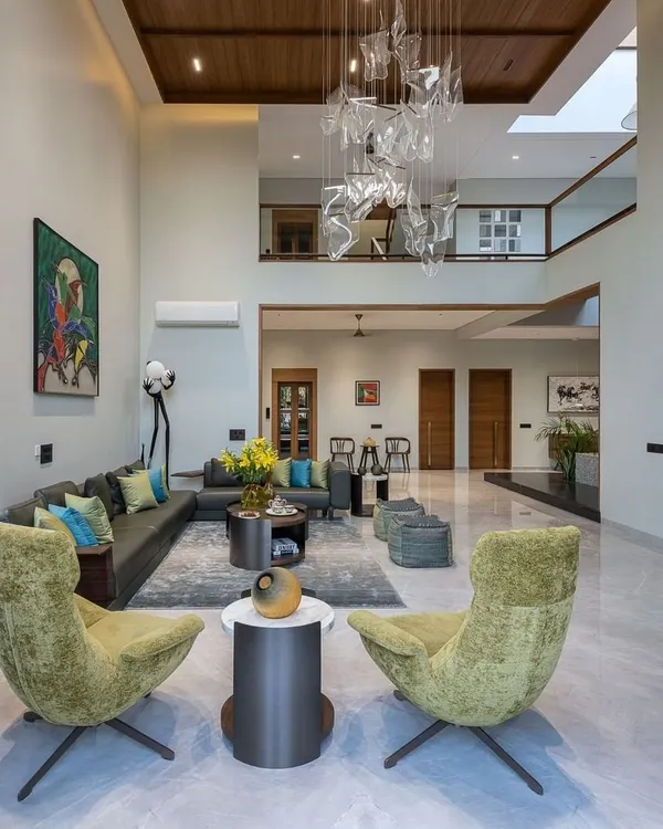This double-height living room is designed for grand impressions and cozy conversations. We used a mix of textures, from the plush green swivel chairs to the cool marble flooring and a statement art piece, creating a space that is both luxurious and welcoming.
