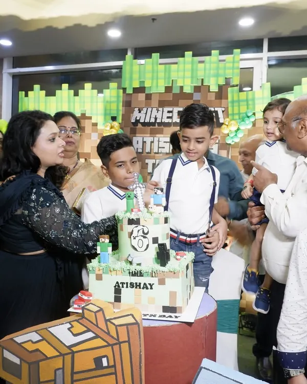 A perfect Minecraft-themed birthday party comes together with a custom cake. Here, the birthday boy, Atishay, is surrounded by family, ready to cut his amazing block-themed cake.