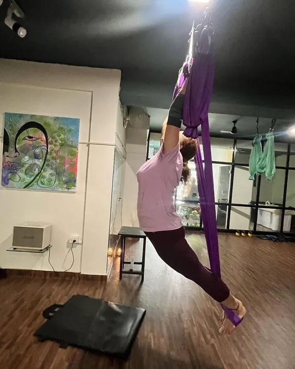 Using the aerial hammock allows for deeper stretches and relieves joint pressure. This image shows a student working on flexibility and strength, supported by the silk.