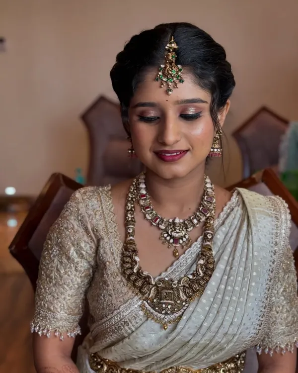 A beautiful makeover for Ramya, the sister of the bride. Her makeup is soft and elegant, designed to complement her stunning antique jewelry and off-white saree.
