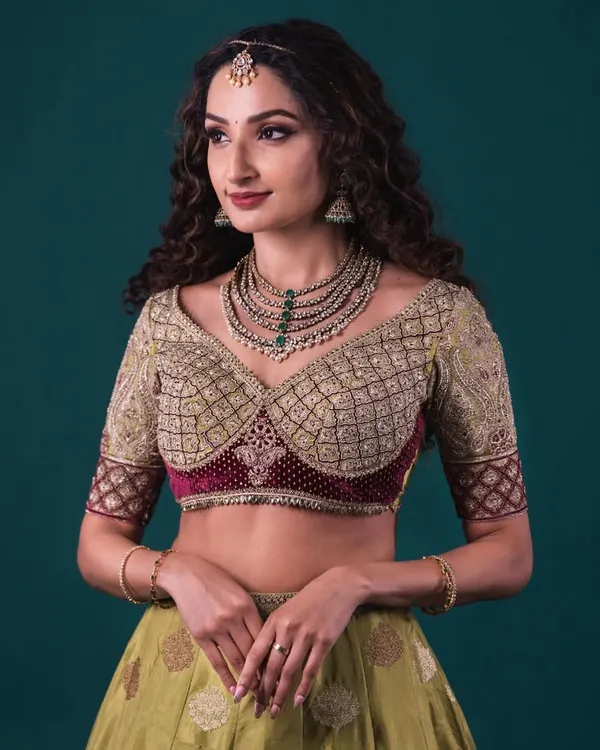A Banarasi lehenga in olive green, paired with a heavily embroidered blouse. The blouse features a unique sweetheart neckline and a contrasting maroon velvet panel.