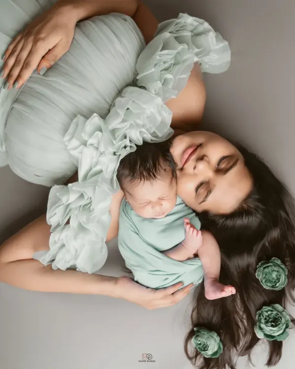 A beautiful overhead portrait of a new mom and her sleeping baby. The soft mint green tones and floral hair accents create a peaceful and artistic image.
