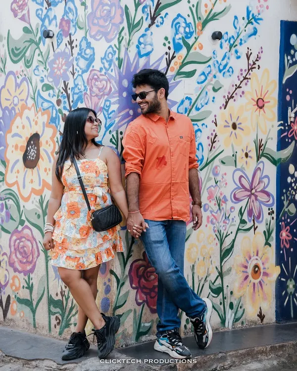 A vibrant and fun pre-wedding shot of a couple posing against a colorful floral mural in Goa, perfectly capturing their playful energy and the lively local art.