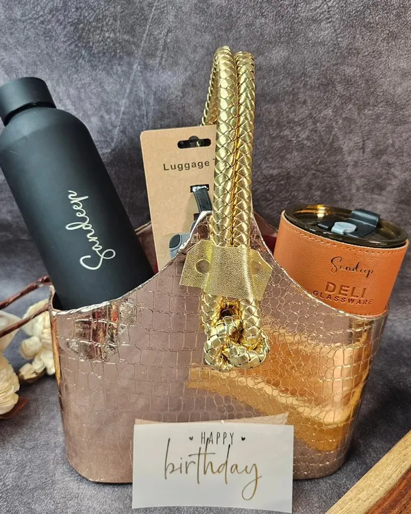 A personalized birthday hamper for your soulmate. This stylish basket includes a custom bottle, a travel mug, and a luggage tag, all in a sleek black and rose gold theme.