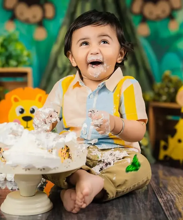 The best part of a cake smash! This little boy is having the time of his life, covered in cake and smiling from ear to ear in a jungle-themed setup.