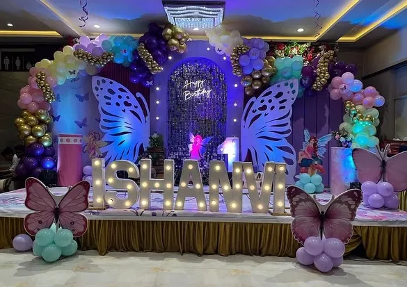 A magnificent butterfly-themed stage for a birthday celebration, featuring large lighted butterfly wings, a custom name sign, and a lush balloon arch in pastel and gold tones. This setup is perfect for a magical, fairytale party.