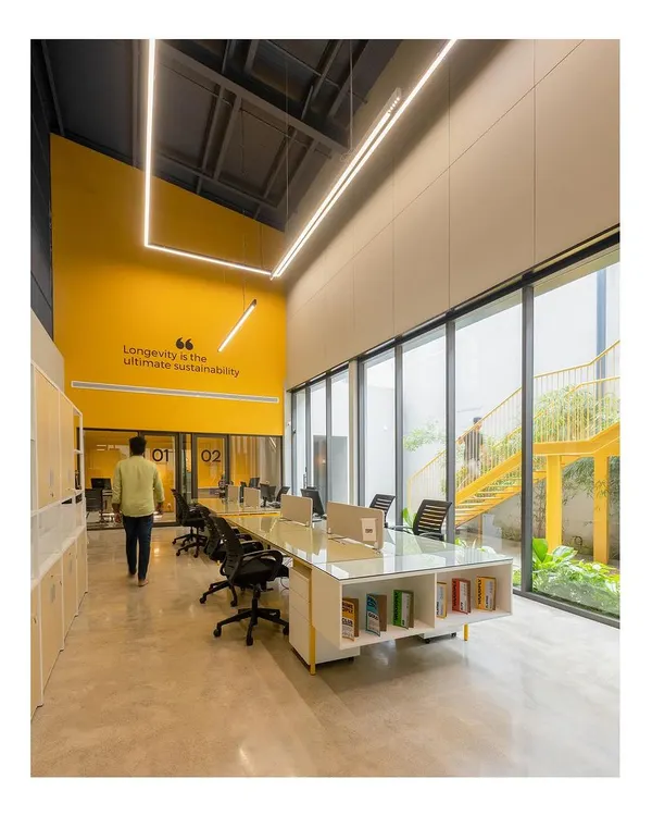 The main workspace at the Prime Ply office features a long, collaborative desk and is flooded with natural light. The design promotes an open, non-hierarchical work culture, with a direct view of the green courtyard.
