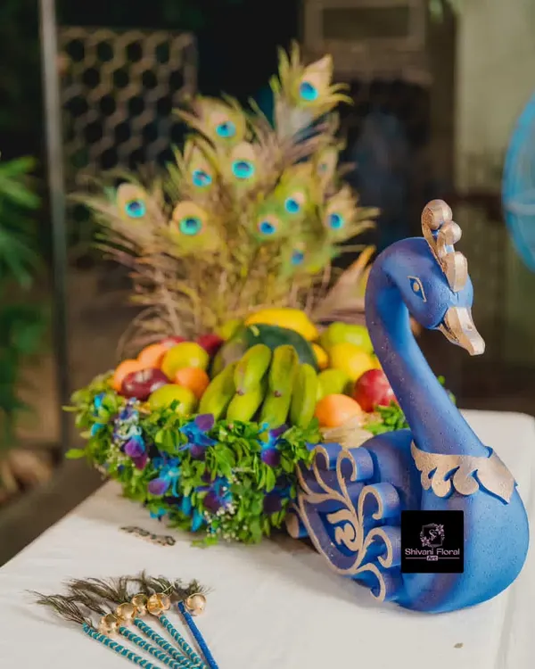 A custom peacock basket, or 'tokri', decorated with fresh flowers and filled with fruits for a baby shower ceremony. The peacock feathers add a touch of royalty.