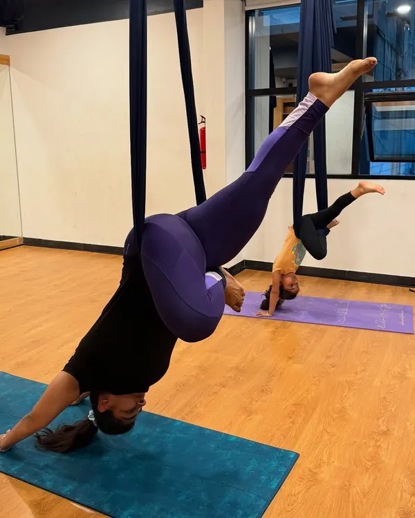 An instructor and a young student practice an inverted pose during an aerial yoga session. This style of yoga is a wonderful activity for families to try together.