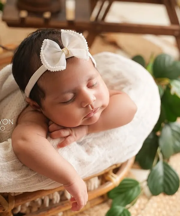 A newborn rests peacefully in a rustic wicker basket, adorned with a simple white bow. This style highlights the baby's natural beauty with earthy textures and soft lighting.
