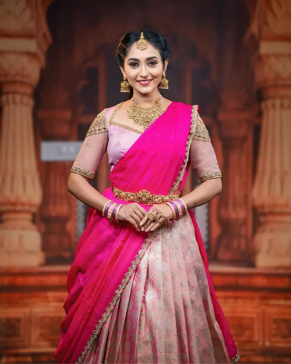 A model looking regal in a pink and cream half saree, paired with our classic matt gold finish choker, earrings, and maang tikka.