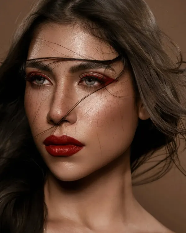 A portrait that is sharp, unapologetic, and real. The wind-swept hair adds a sense of movement and raw energy, contrasting with the precise, crimson makeup. This is editorial beauty that captures both strength and vulnerability.