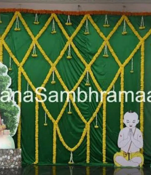 A traditional backdrop for a sacred thread ceremony (Upanayanam). The decor uses green drapes with marigold lattice work and features cutouts representing the religious theme.