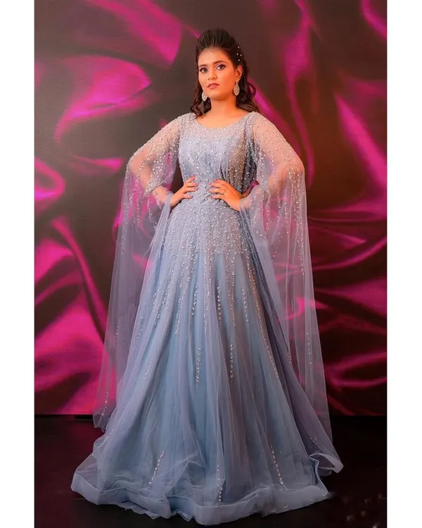 Feel like a modern Cinderella in this stunning powder blue gown. The sparkling details and elegant cape sleeves make it a magical choice for any reception or engagement party.