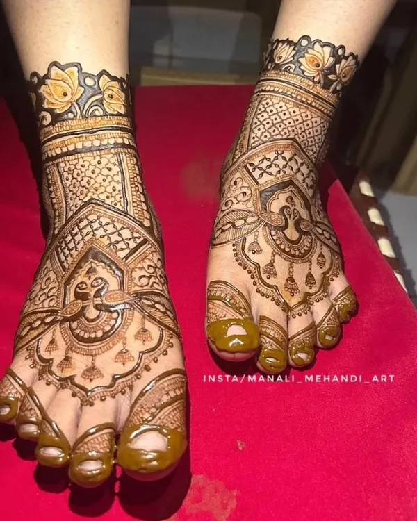 A close-up of a bridal foot mehandi design. The pattern covers the entire foot with a mix of traditional motifs and fine line work, ending with a floral cuff.