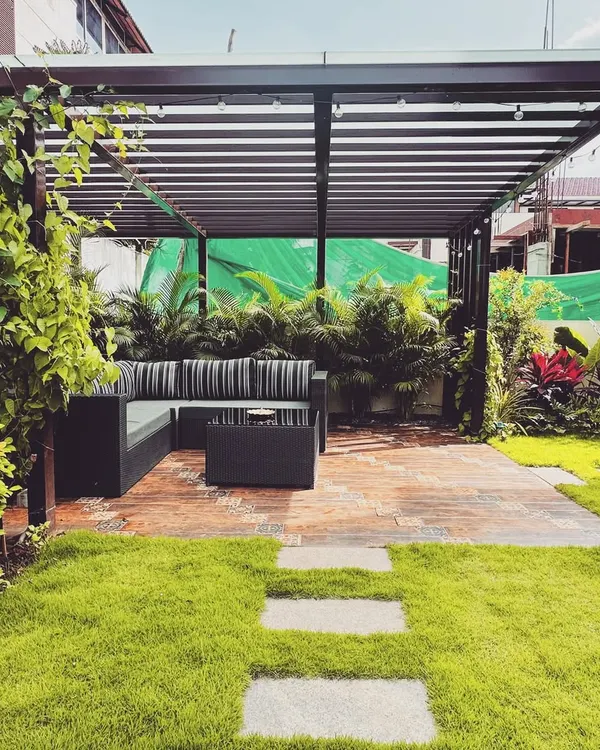A modern metal pergola defines this comfortable outdoor lounge area. The slatted roof offers partial shade while maintaining an open, airy feel, creating a perfect spot for seating nestled within the garden.