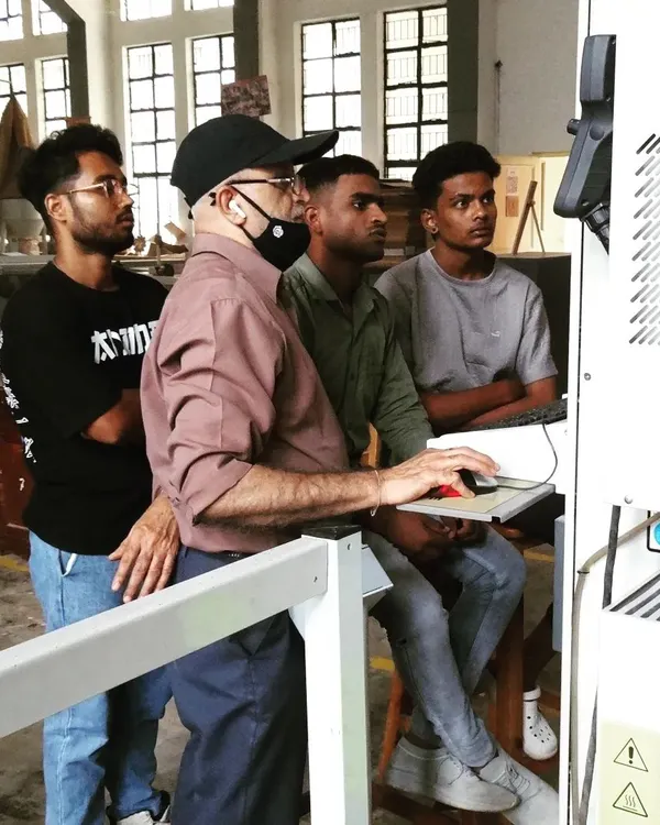 An instructor and students review a program on the CNC machine's control panel. This is where digital designs are translated into machine commands.