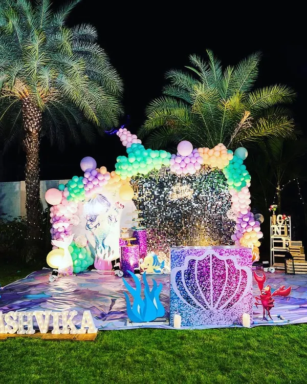 This outdoor Mermaid theme birthday party is one of my favorites. The setup includes a large, sparkling sequin backdrop for the stage, a custom balloon arch with sea-inspired colors, and unique props like a glittery seashell and coral cutouts to create a complete underwater fantasy.