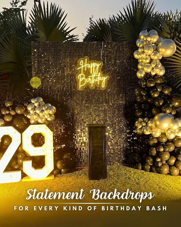 A statement backdrop for a 29th birthday bash. This outdoor setup features a bold black and gold balloon arrangement against a shimmering sequin wall, complete with marquee numbers to mark the special year.