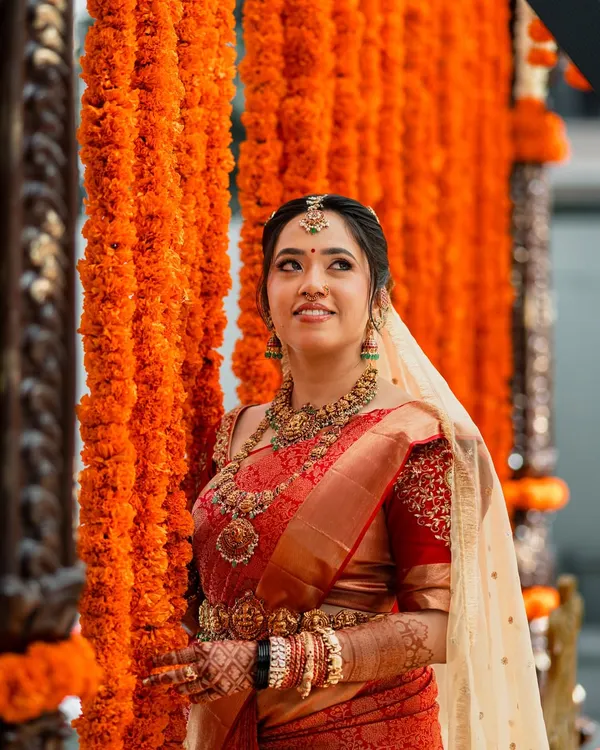 A breathtaking vision in red, this bride embodies traditional South Indian grace. Her look features classic temple jewellery and a radiant makeup look with defined eyes and a bold lip, perfectly complementing her vibrant Kanjivaram saree.
