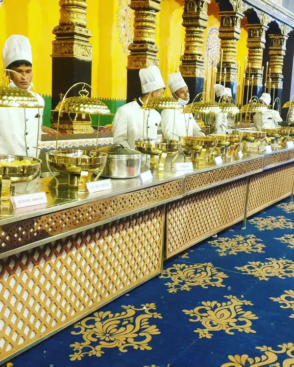 A view of our traditional 'Rajwadi' buffet line, featuring our uniformed staff ready to serve. The combination of ornate golden pillars in the venue and our polished brass dishes creates an unforgettable, regal dining atmosphere for your wedding.