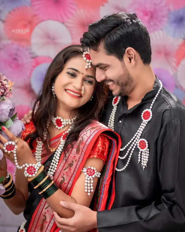 A couple dressed for Makarsankranti shares a candid, smiling moment against a backdrop of purple and pink flowers. These couple portraits capture the joy of the festival.