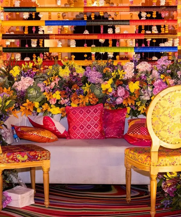 A burst of color for a Mehendi seating area, featuring a backdrop of multi-colored panels and a profusion of vibrant flowers, set against the royal architecture of Shiv Niwas Palace.
