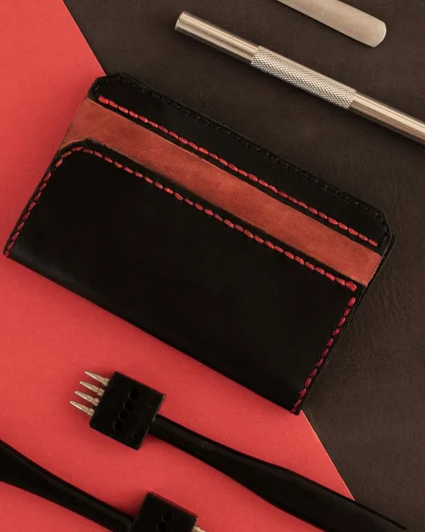 The essential tools for leatherworking laid out next to a finished cardholder. In our workshop, you'll learn to use these tools to cut, punch, and stitch leather into a professional-quality product.