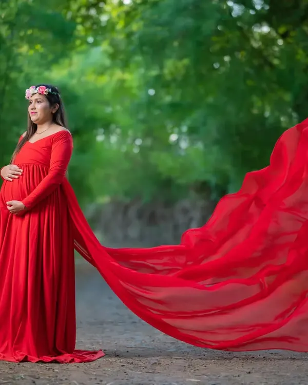 The drama of a long, flowing red gown looks incredible outdoors. The fabric catches the light and breeze, creating a stunning contrast against the natural green background of this rustic path.