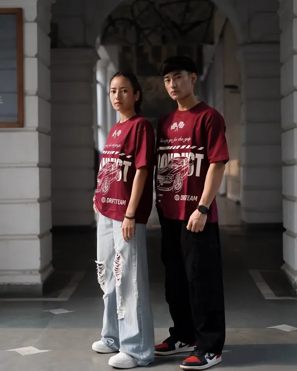 A shot featuring both male and female models to showcase the unisex appeal of the graphic tee. The symmetrical pose in this architectural corridor creates a strong, balanced image for a brand campaign.