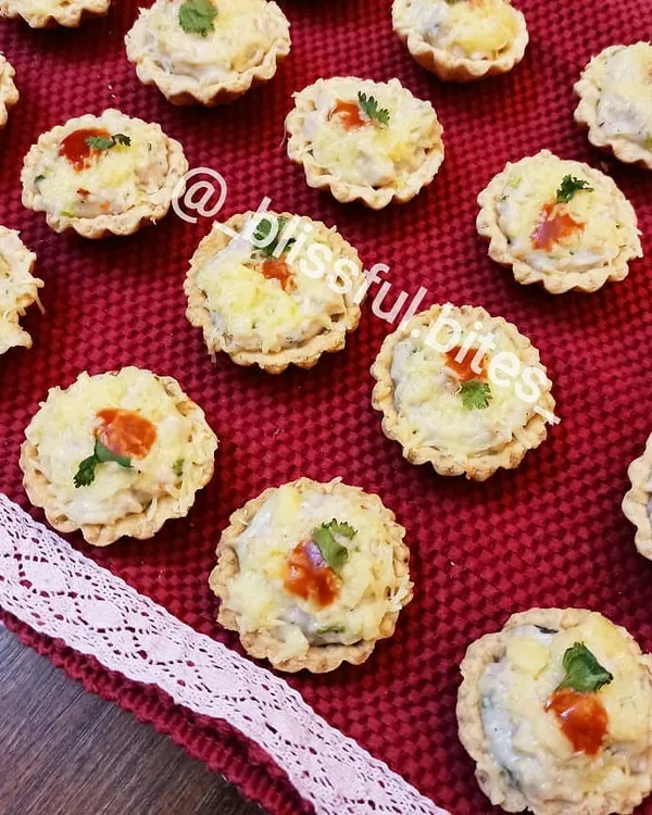 A tray of my freshly baked Creamy Chicken and Cheese Tarts, garnished with a bit of chili sauce and cilantro. These savoury tartlets are a hit at any event.