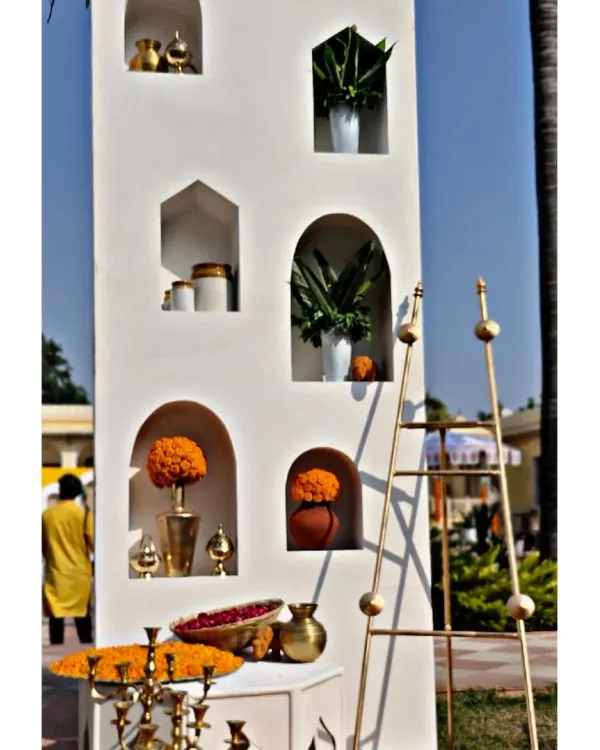 A detail of the Haldi ceremony entrance, showing the clean white structure with arched niches filled with marigold arrangements and brass pots. This is how we blend modern design with traditional elements.