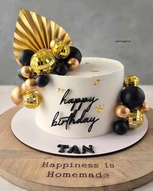 A chic black and gold birthday cake. The clean white whipped cream provides a perfect canvas for the mini disco balls and gold fan accent.