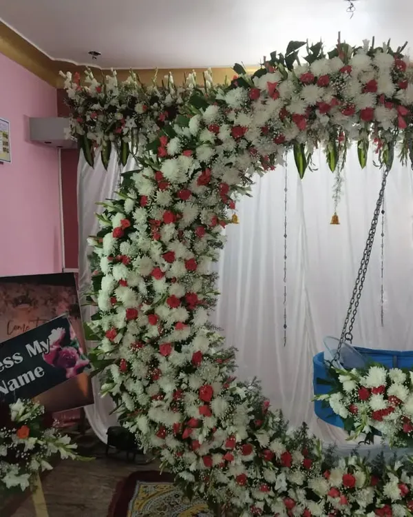 A full view of our highly requested naming ceremony decor. This design features a large crescent moon arch covered in white and red flowers, with a beautifully decorated cradle (thottilu) suspended in the center.