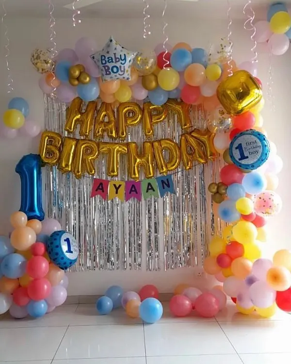 A classic birthday decoration perfect for a living room. This setup includes a 'Happy Birthday' foil balloon banner, a shimmer curtain, and a colorful balloon frame.