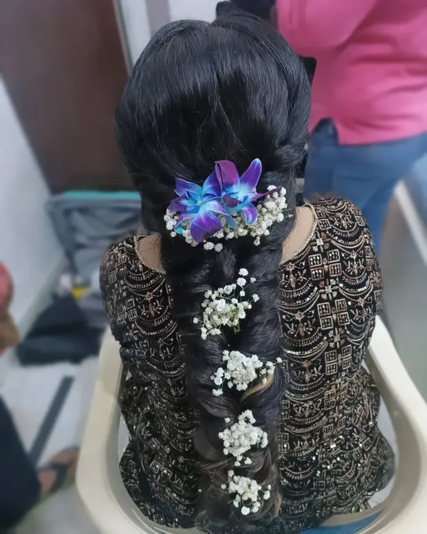 An intricate fishtail braid adorned with fresh baby's breath and vibrant purple orchids. This is a stunning and unique hairstyle for a Mehendi or Sangeet ceremony.